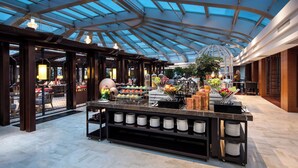 A spacious atrium with a high glass ceiling, a central buffet area with various food items, and a seating area with tables and chairs. - Ascott Riverside Garden Beijing (Beijing)