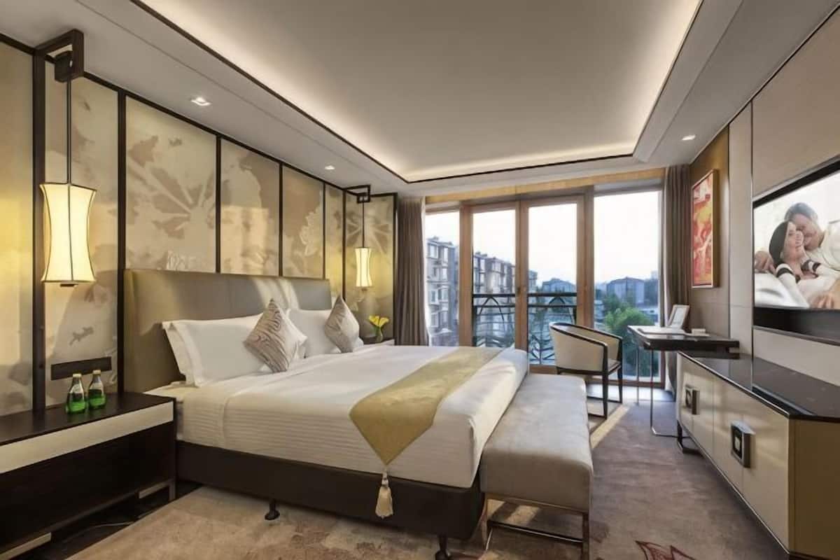 Una habitación de hotel moderna con una cama grande, mesitas de noche, un televisor y un balcón con vista a la ciudad.