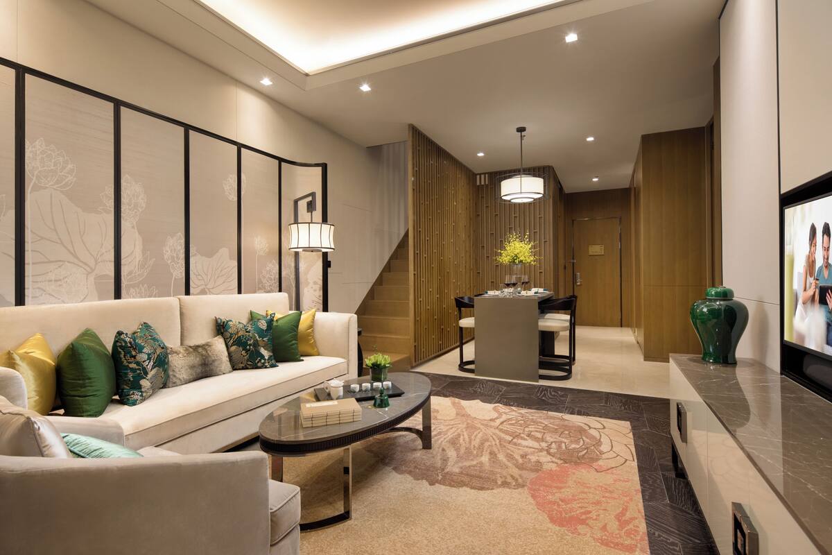 Una sala de estar moderna con sofá, una mesa de centro y televisión. Se ve una escalera que conduce a otra habitación.