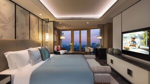 A modern hotel room with a large bed, a desk, a chair, a television, and a view of the cityscape through large windows. - Ascott Riverside Garden Beijing (Beijing)