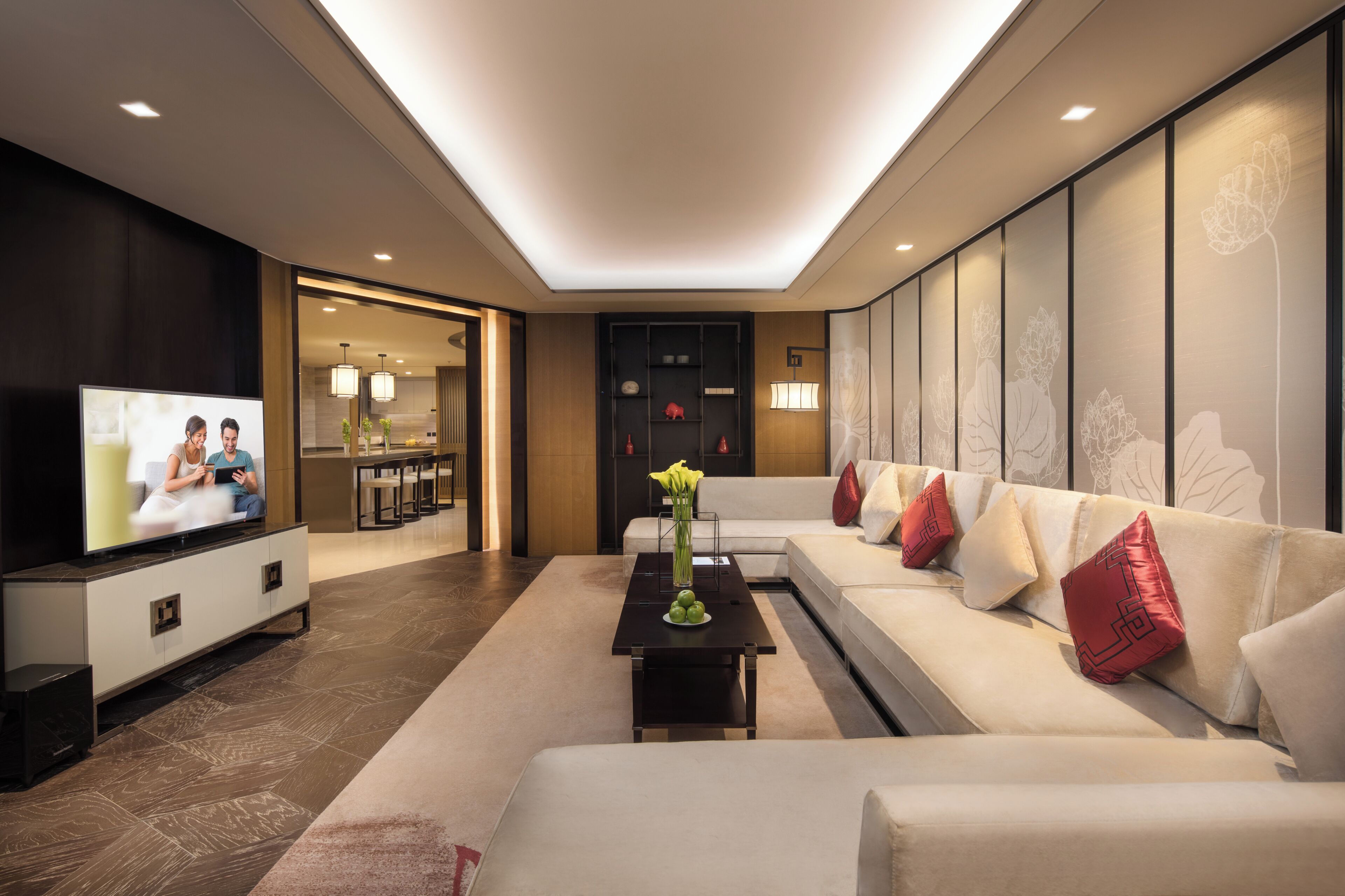A modern living room with a sofa, a coffee table, and a TV. There is a kitchen area in the background.