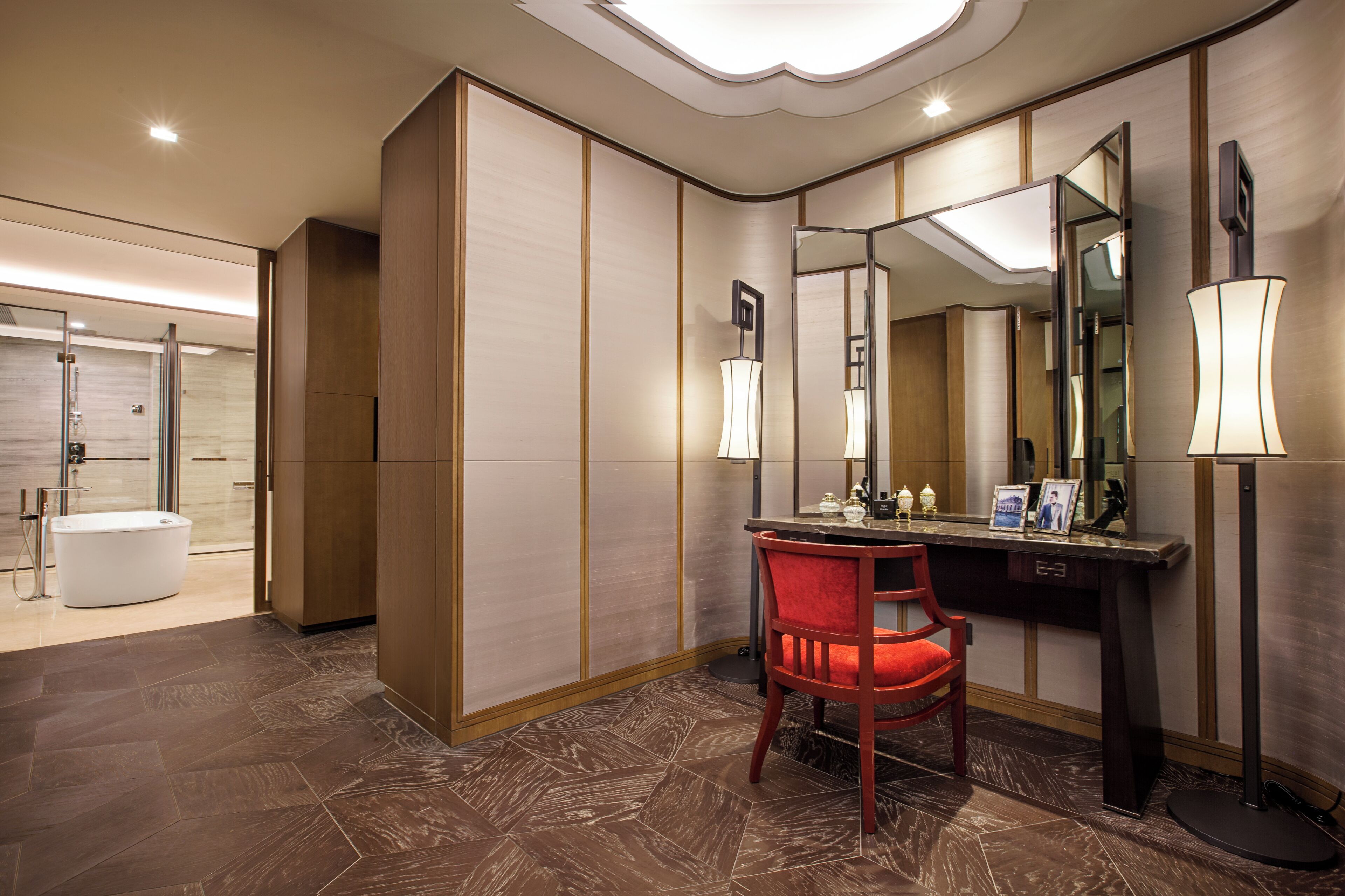 A modern bathroom with a large mirror, a vanity with a red chair, and a separate shower area.