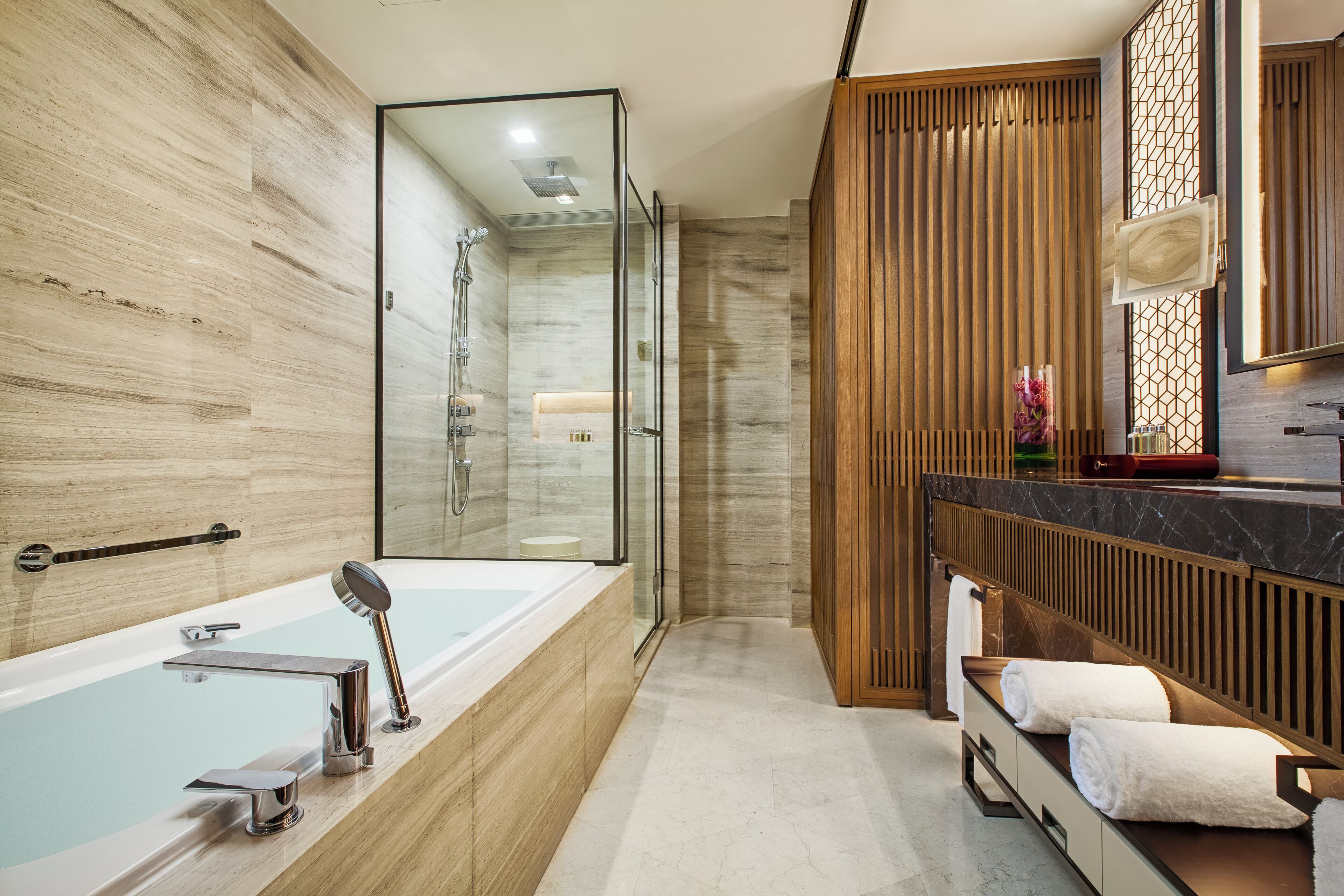 A modern bathroom with a large bathtub, a glass-enclosed shower, and a wooden vanity with a mirror.