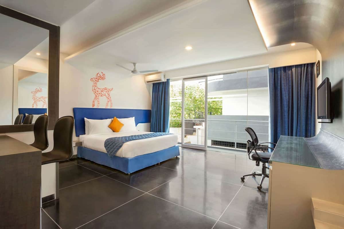 A modern hotel room with a large bed, a desk, a chair, a TV, and a balcony with curtains.