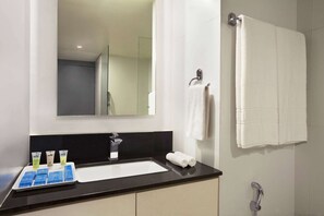 A modern bathroom with a black countertop, a white sink, and a mirror above it. There are three toiletries on the counter and a towel hanging on the wall. - Days Inn & Suites by Wyndham Bengaluru Whitefield (Bengaluru)