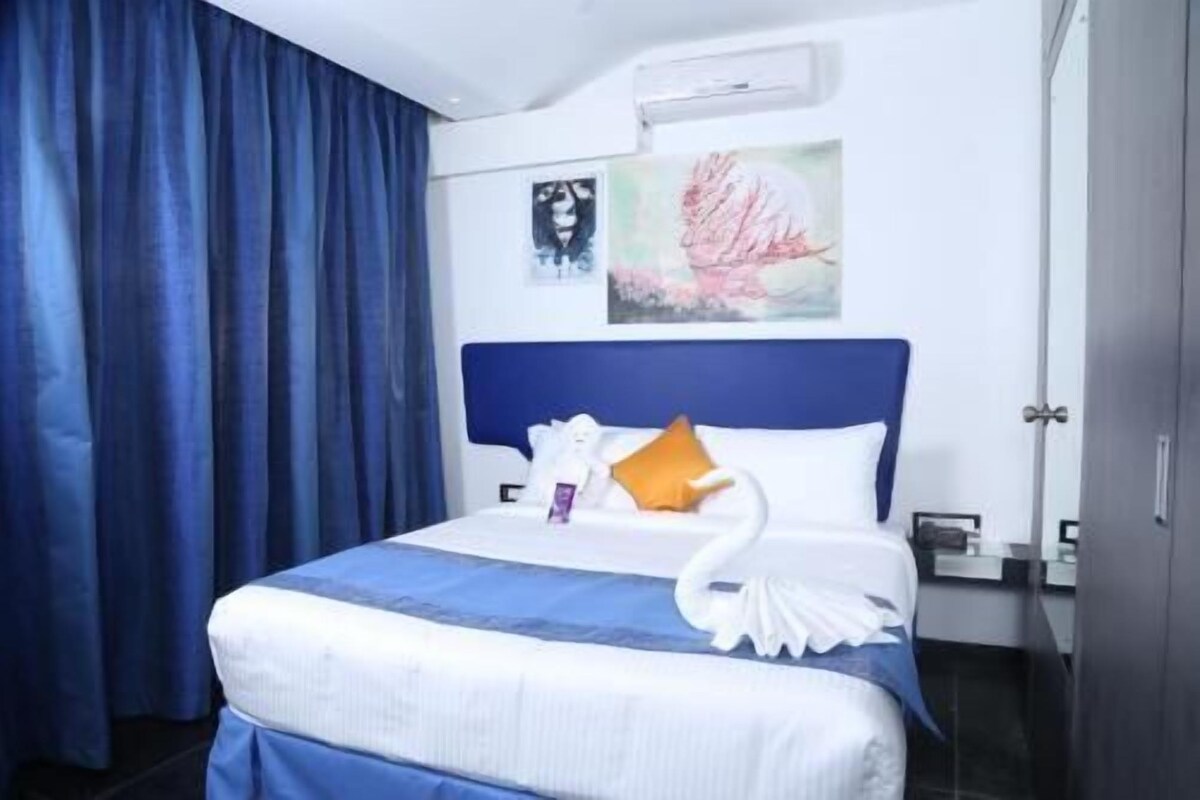 Habitació d'hotel amb un llit, un panell cefalòtic blau, una decoració d'un cigne blanc, un quadre i una cortina blava.