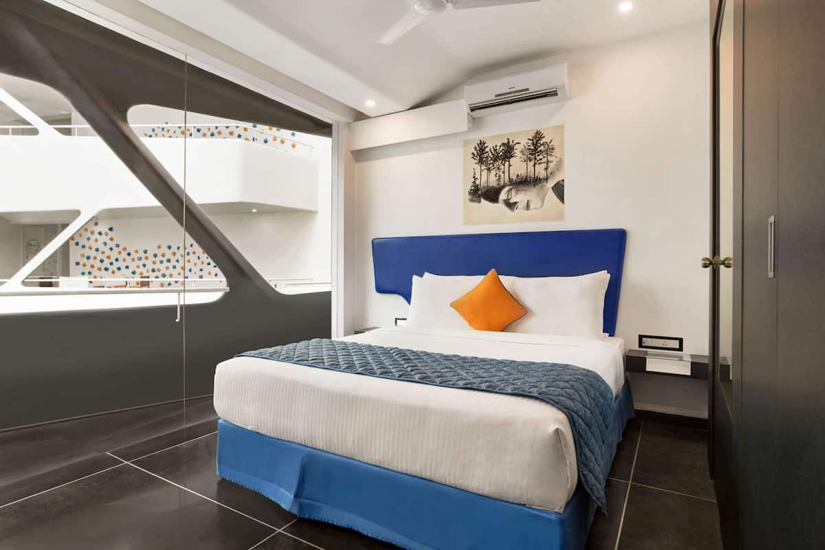 A modern bedroom with a large bed, a blue headboard, and a view of a balcony with a geometric design.