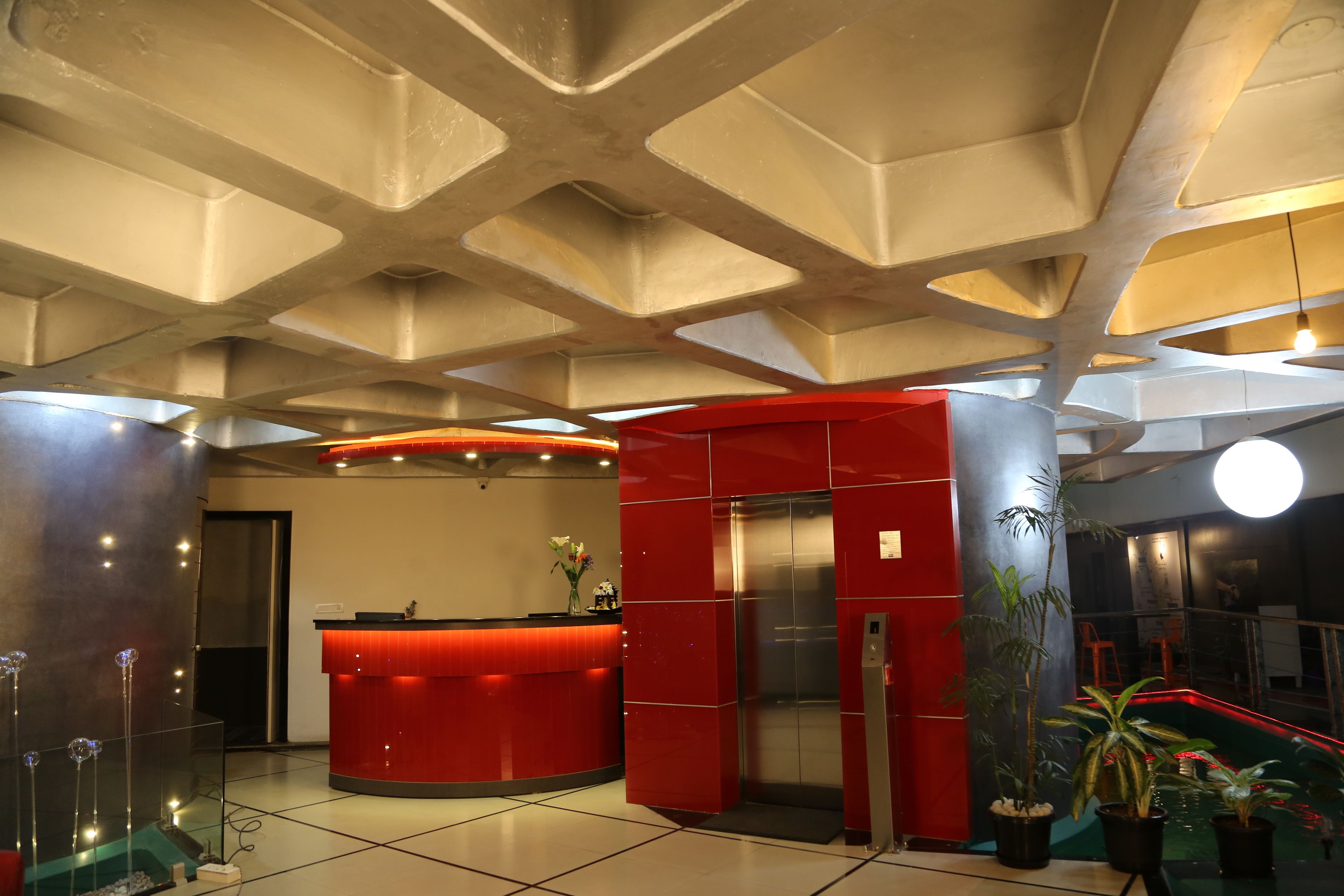 A modern lobby with a red reception desk, a staircase, and a large potted plant.