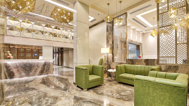 Un hall con mostrador de recepción, sofás verdes, suelo de mármol e iluminación decorativa.