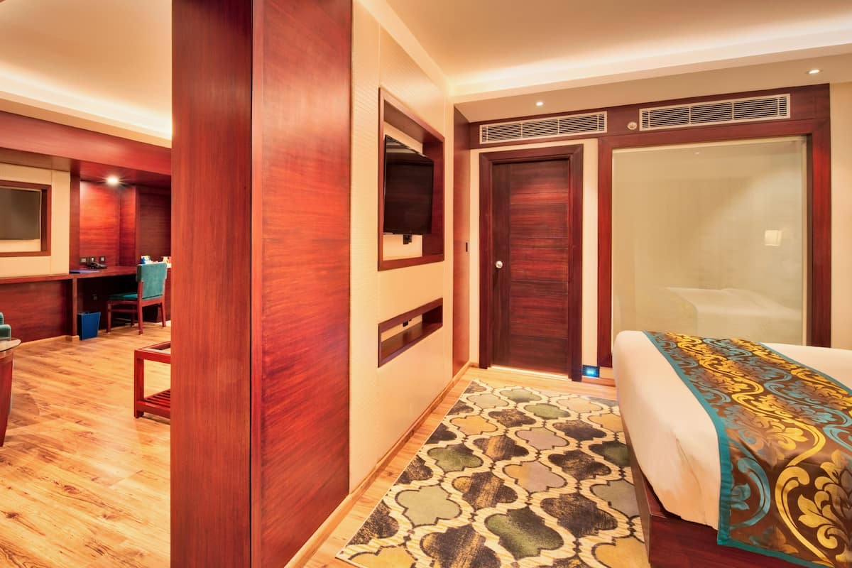 A hotel room with a large bed, a desk with a chair, a TV mounted on the wall, and a bathroom with a large mirror and a shower.