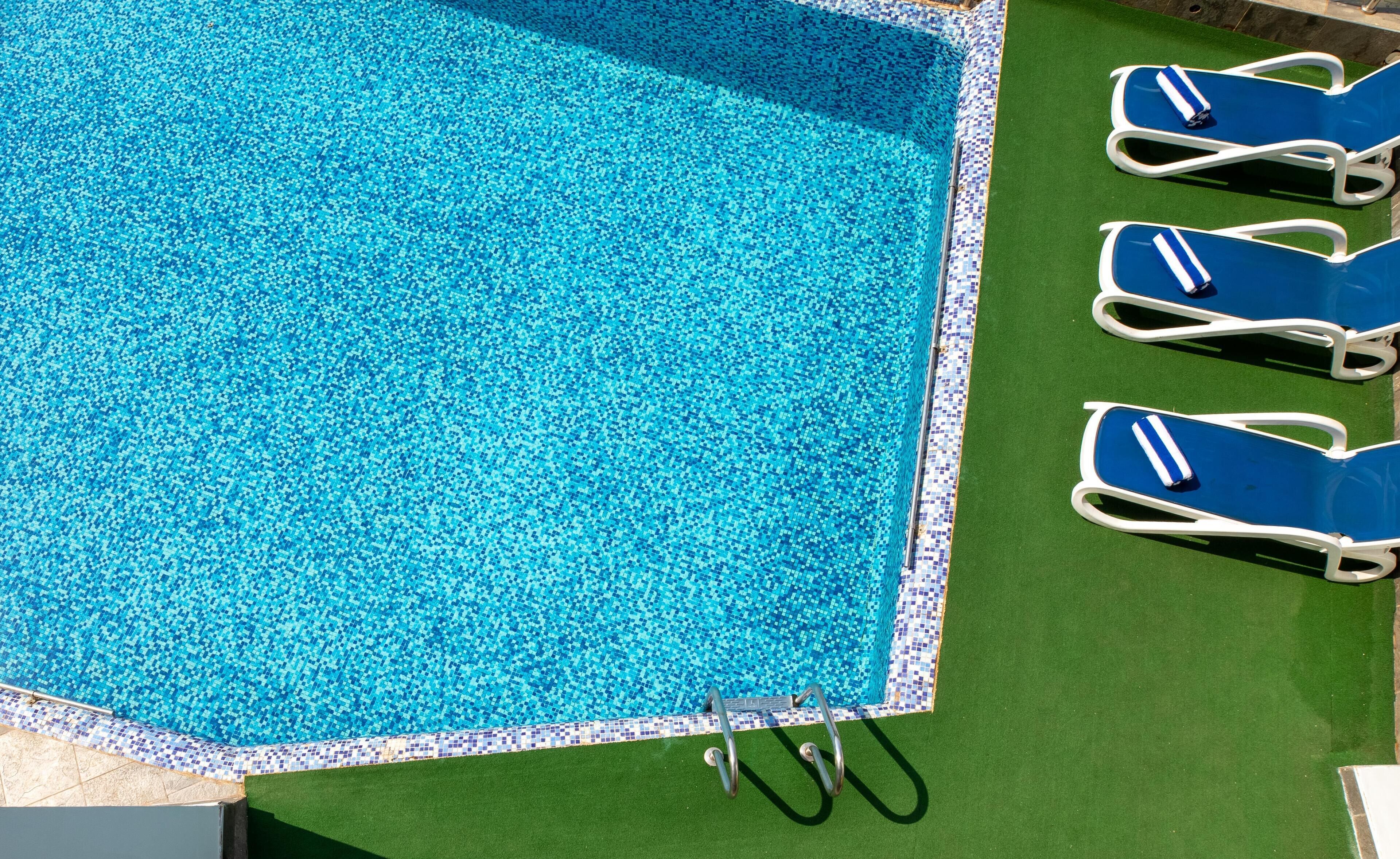 A swimming pool with a tiled edge and a green lawn area.