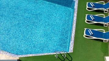 A swimming pool with a tiled edge and a green lawn area.