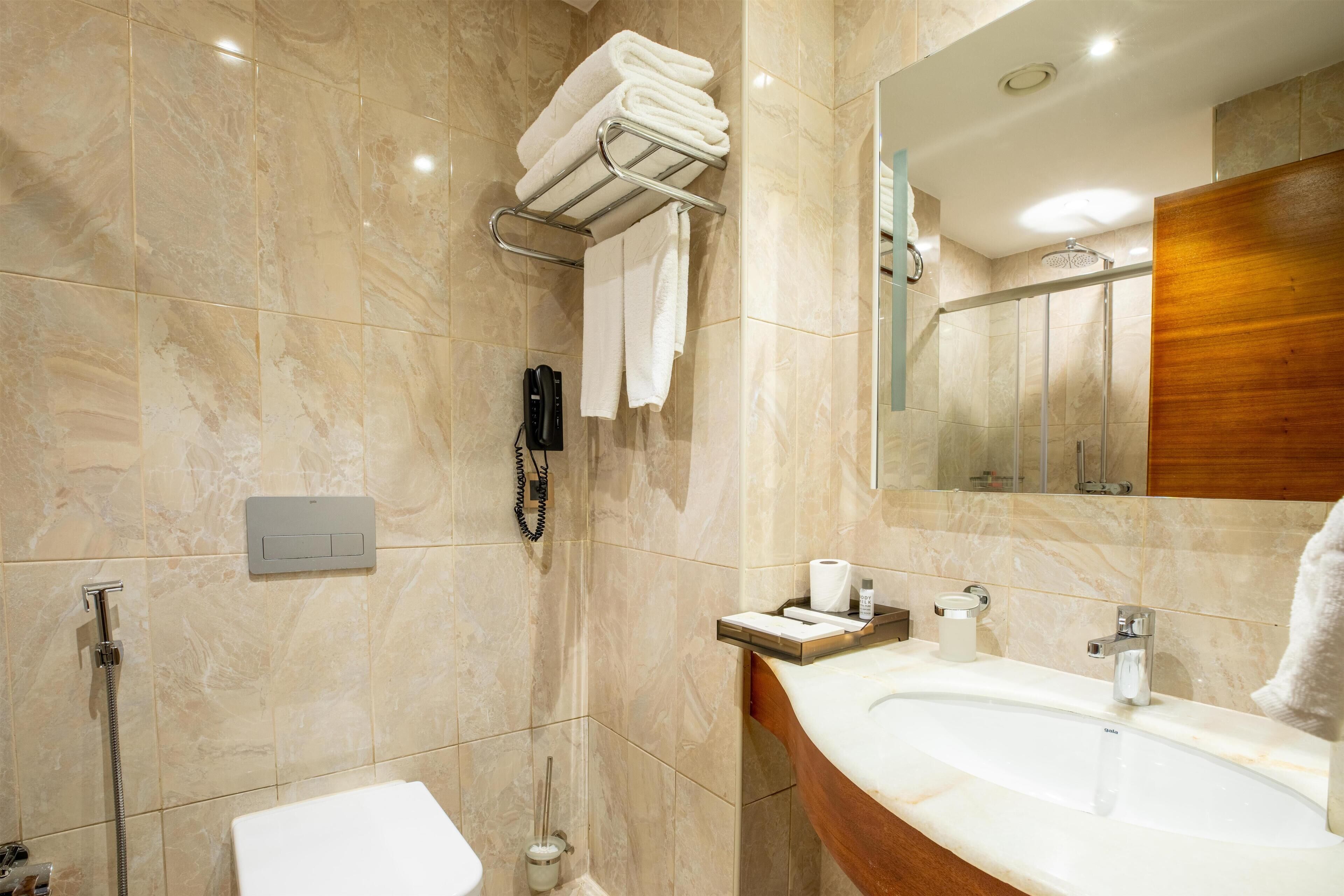 Un baño moderno con piso de mármol, un lavabo con tocador de madera, un espejo y un perchero para toallas.