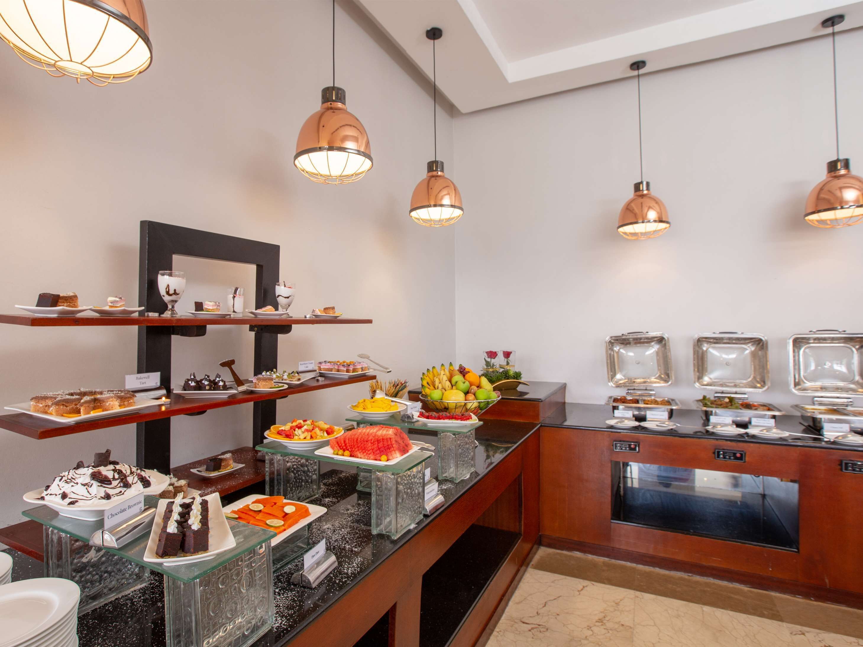 A buffet with various desserts and fruits, glass display cases, and hanging pendant lights.
