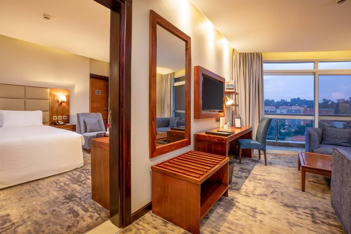 Hotelkamer met een groot bed, een bureau, een stoel, een bank, een televisie en een groot raam met uitzicht op de stad.