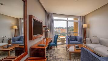A hotel room with a large window, a flat-screen TV, a desk, two sofas, and a coffee table.