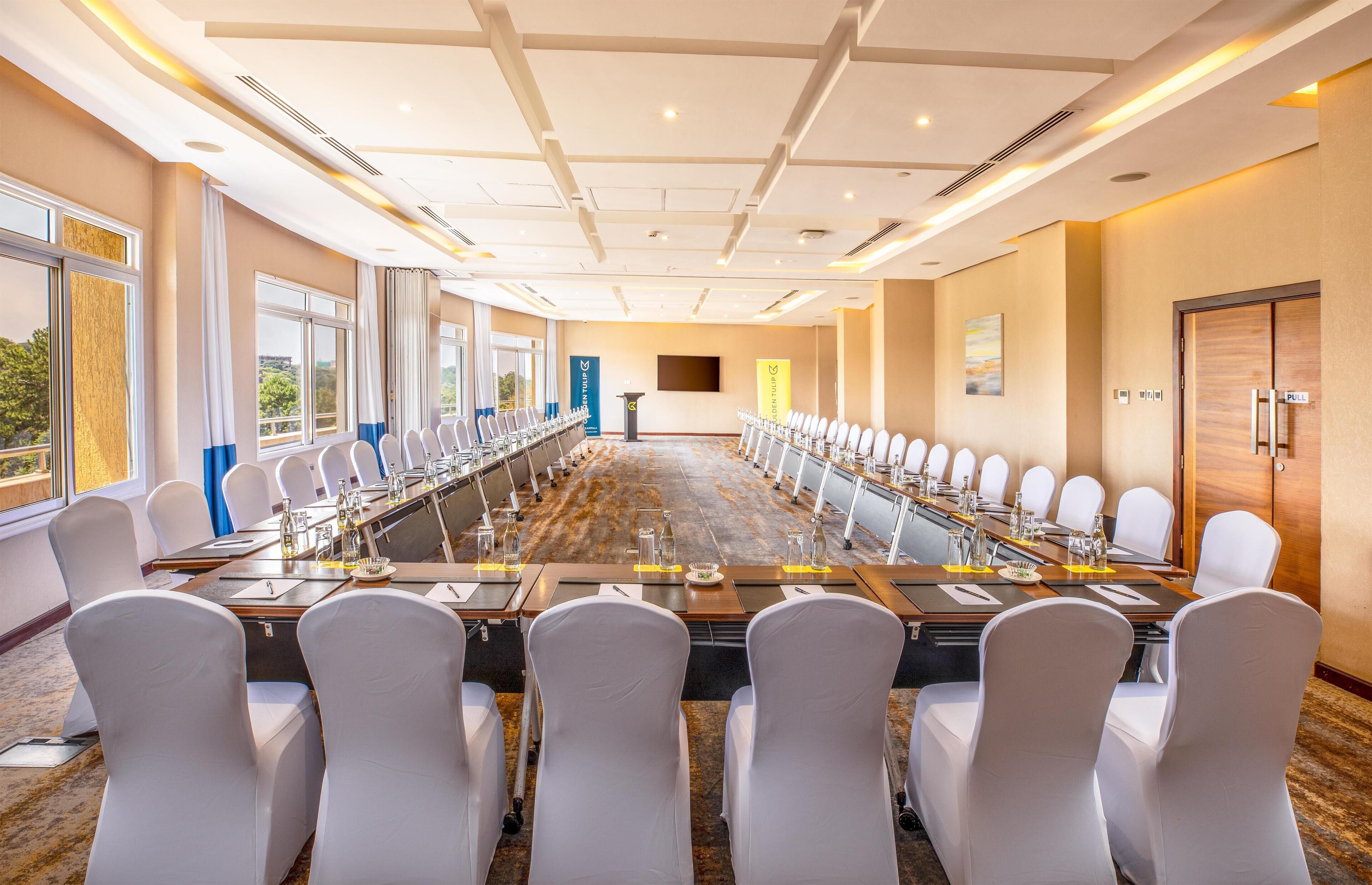 Une salle de conférence avec une longue table, des chaises blanches et un pupitre.