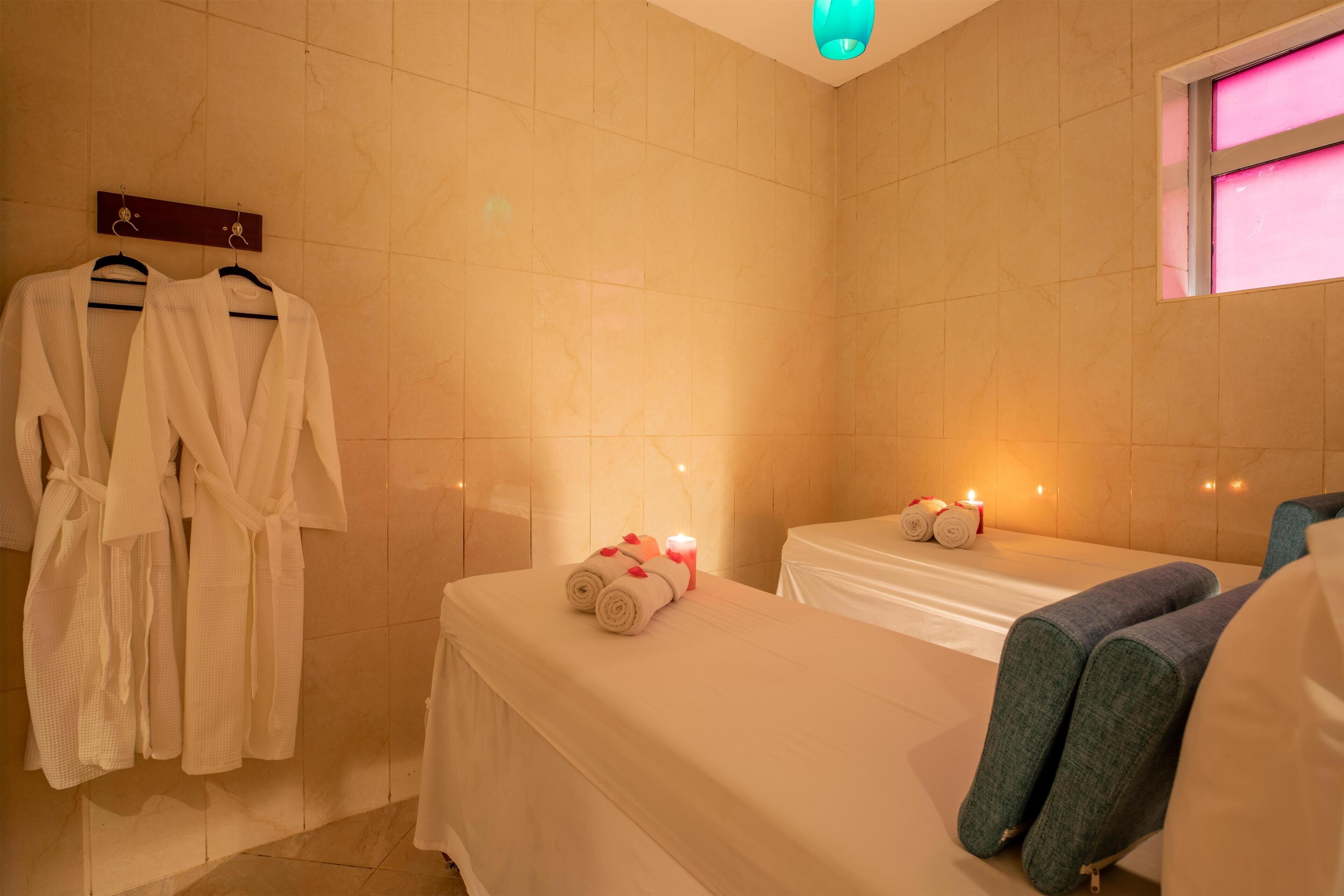 A spa room with two beds, towels, and robes on hangers.