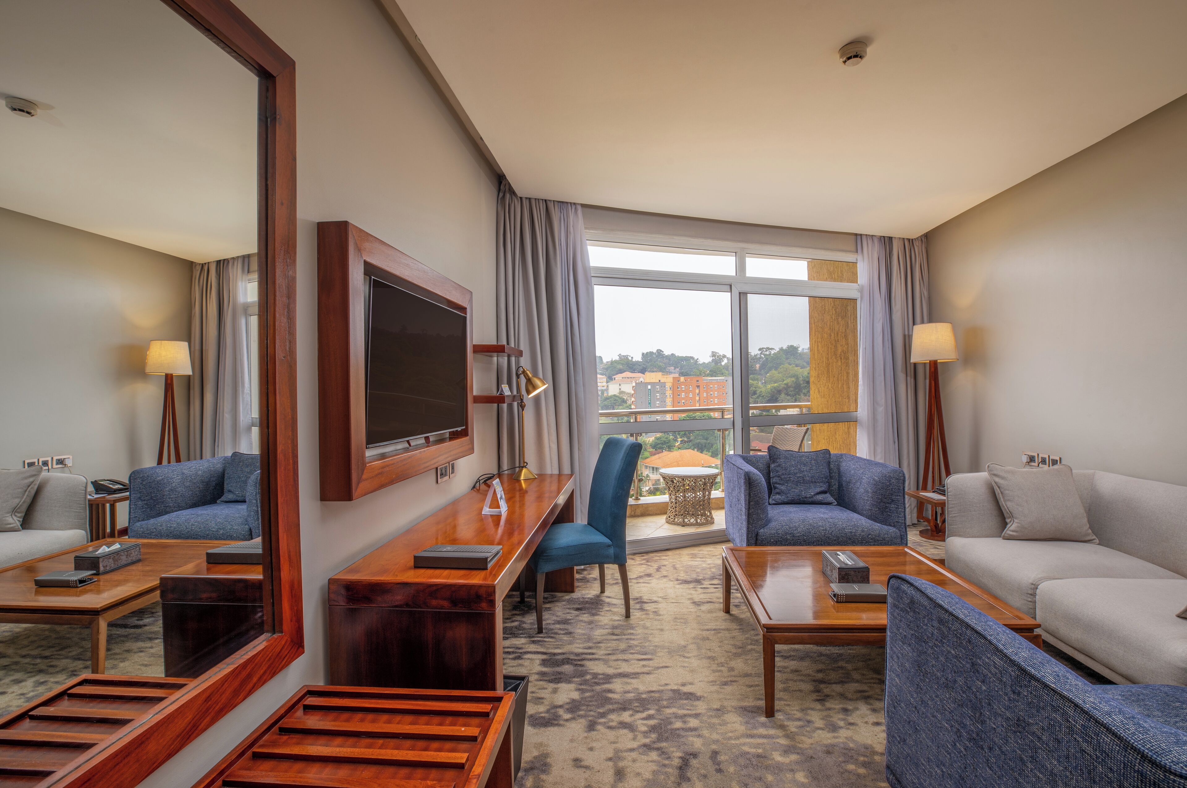 A hotel room with a large window, a flat-screen TV, a desk, two sofas, and a coffee table.