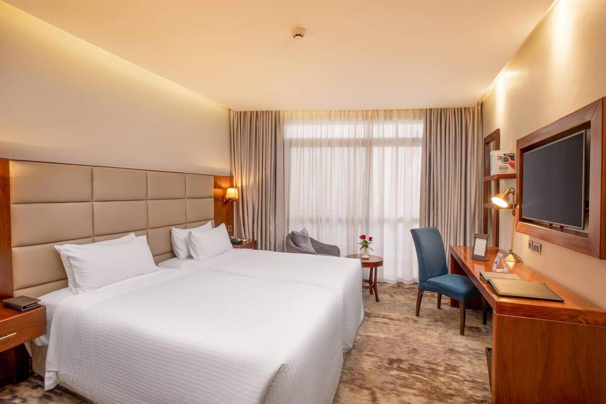 Een hotelkamer met een groot bed, een bureau met stoel, een televisie en een kleine tafel met lamp.