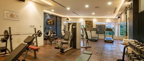 Un gimnasio bien equipado con diversas máquinas de ejercicio, estantes para pesas y bancos.