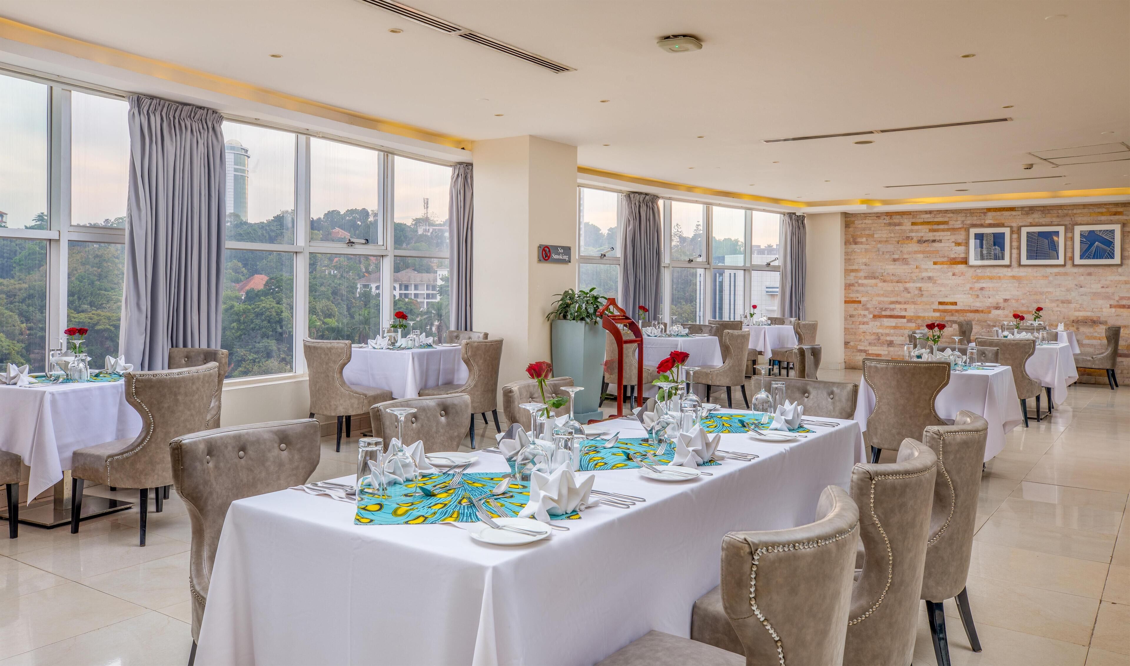 A restaurant with multiple tables set for dining, large windows with curtains, and a view of the cityscape.