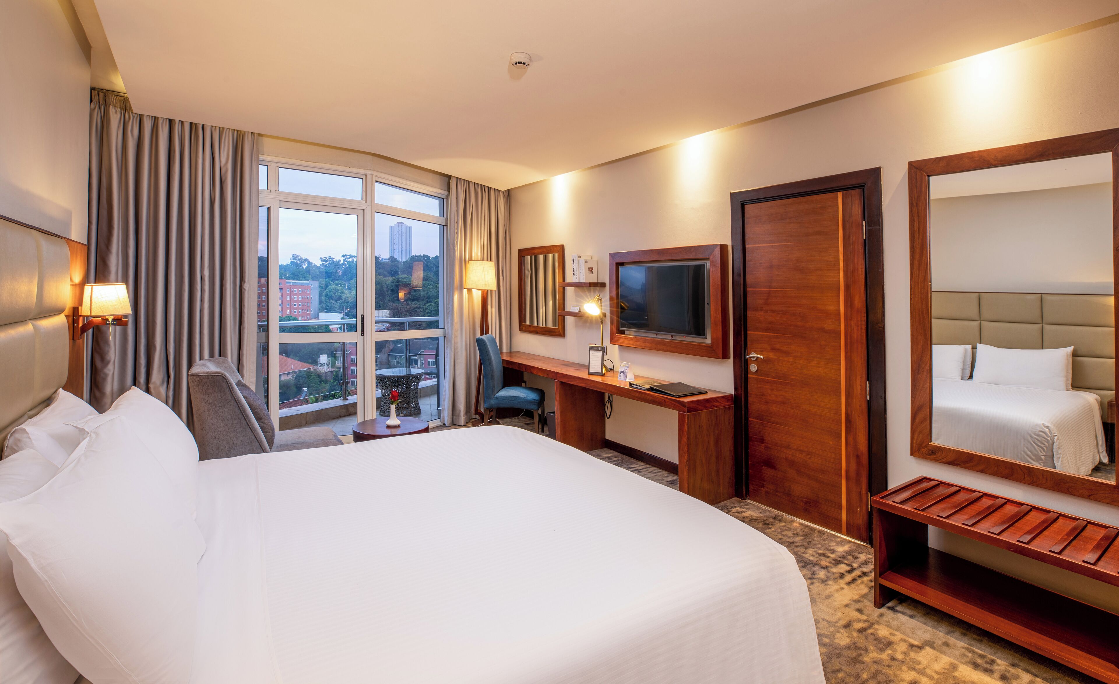 Una habitación de hotel con una cama grande, un escritorio con una silla, un televisor y una ventana con cortinas.