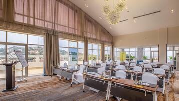 A conference room with tables, chairs, and a podium, large windows with curtains, and a city view.