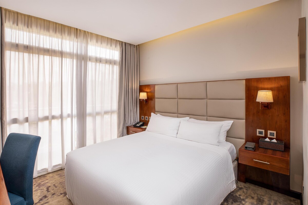 Habitación de hotel con una cama grande, un escritorio con silla, una mesita de noche con lámpara y un teléfono instalado en la pared.