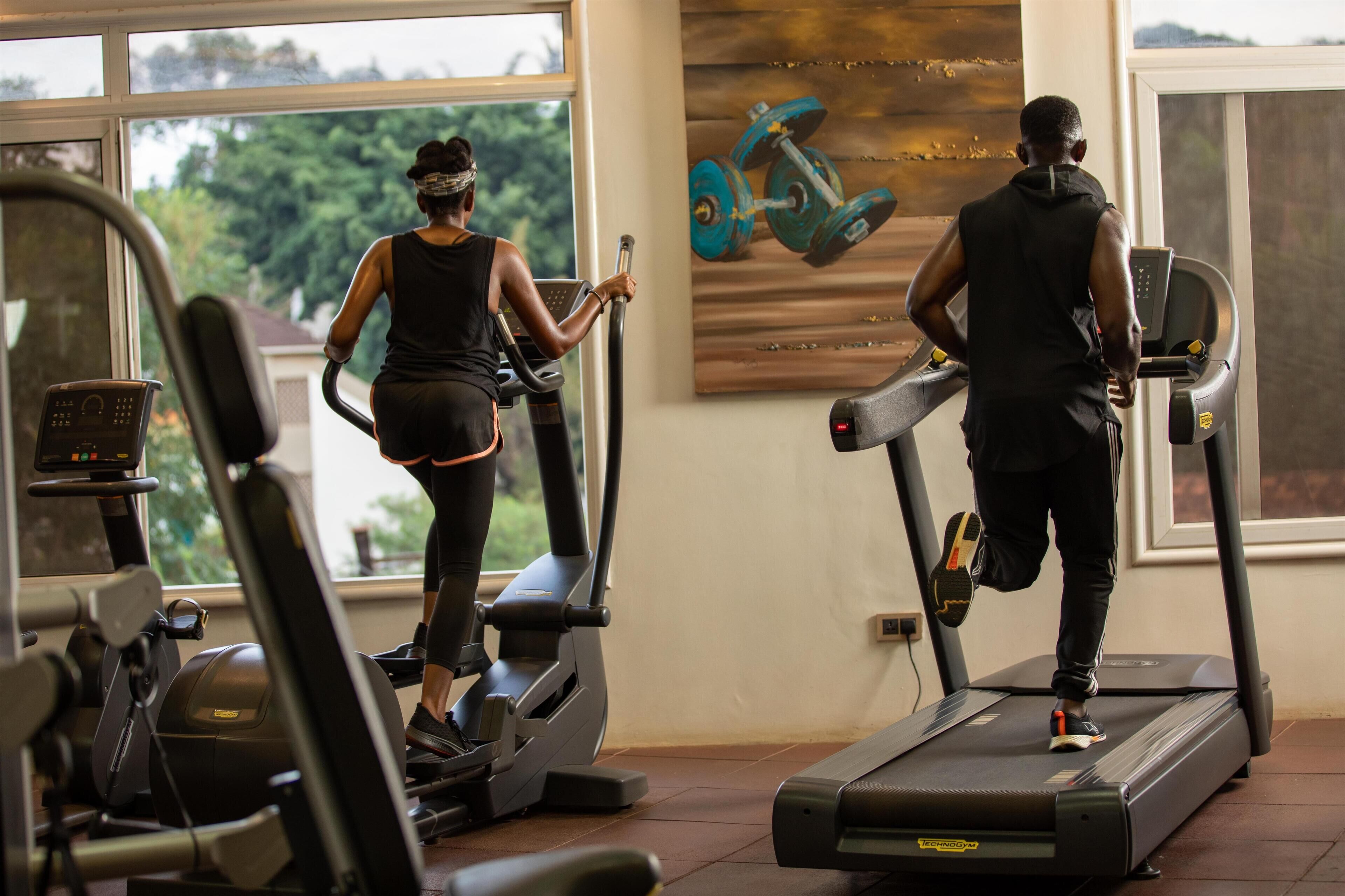 A gym with treadmills, stationary bikes, and a wall with a painting.