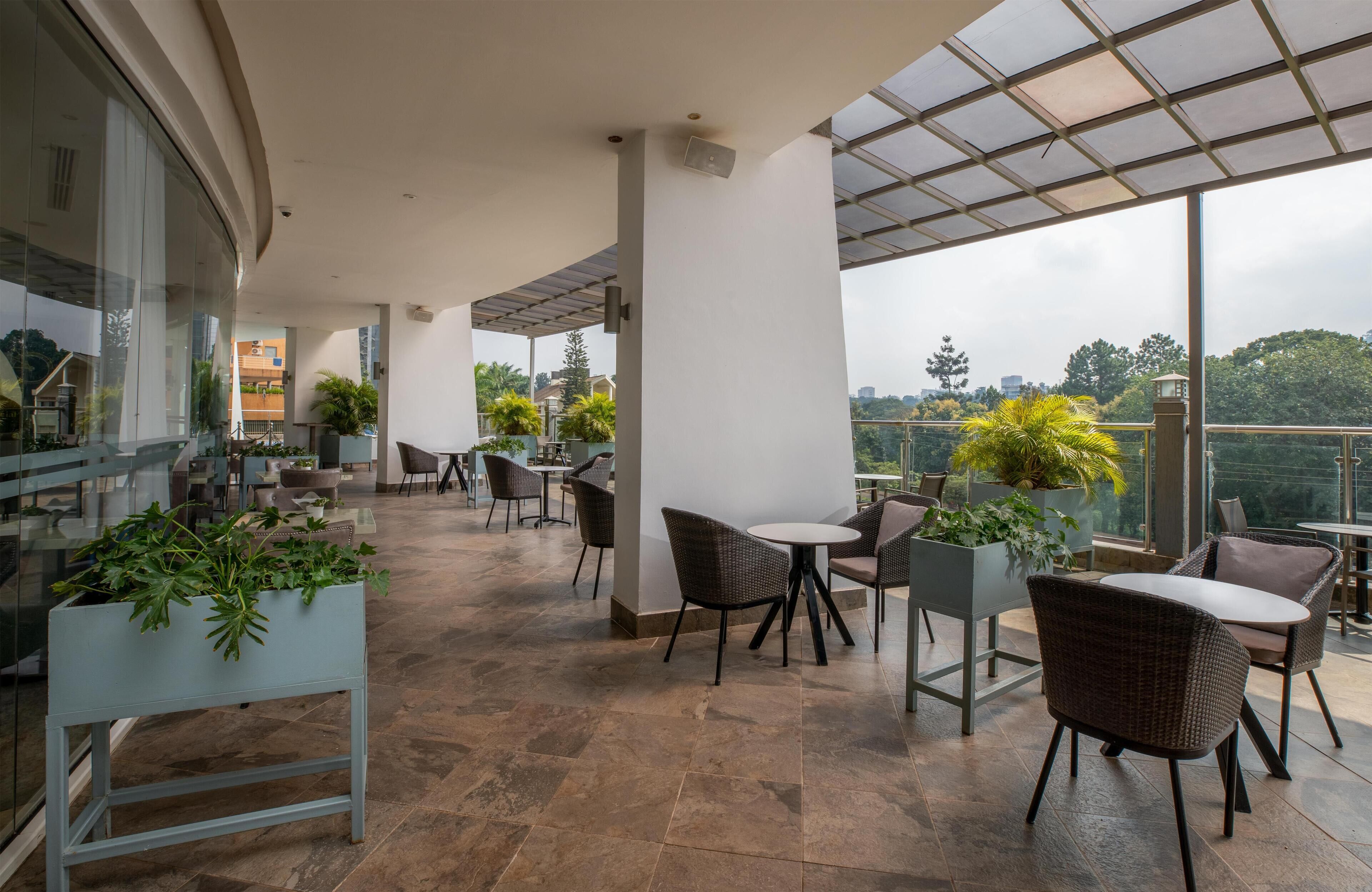 A spacious outdoor patio with modern wicker furniture, potted plants, and a glass ceiling offering a view of the cityscape.