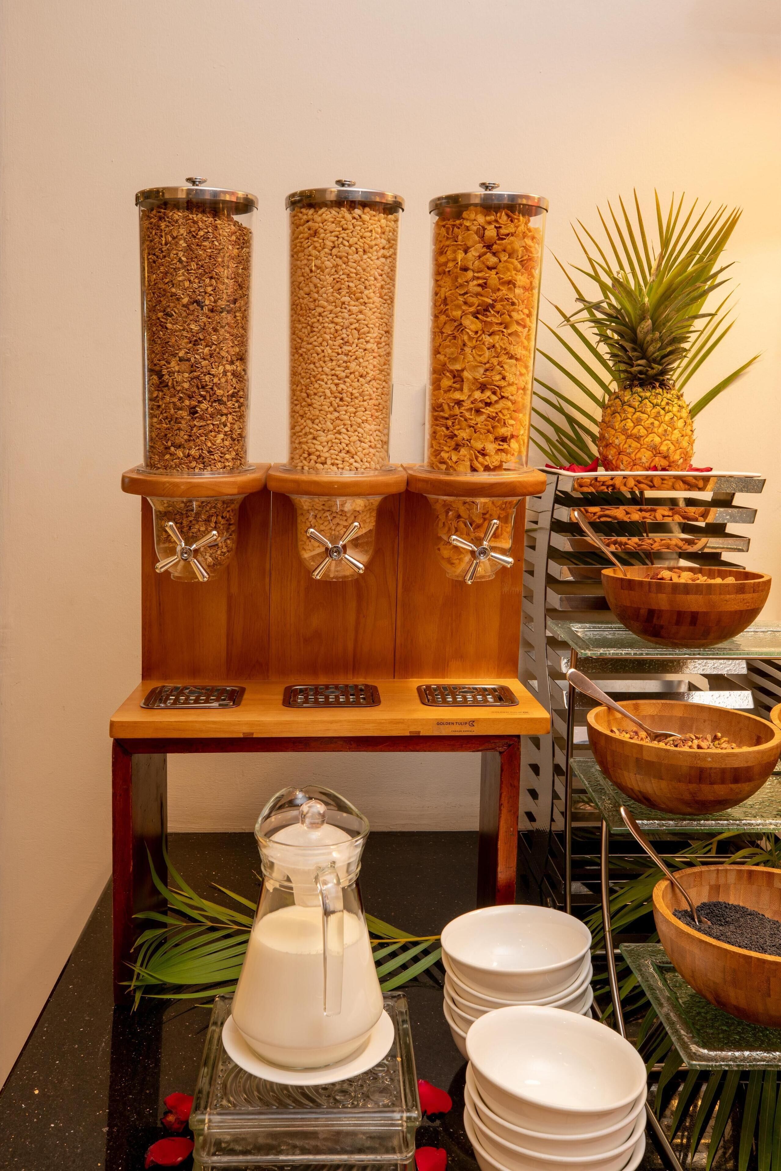A breakfast buffet setup with three dispensers, a pineapple, and a milk pitcher.