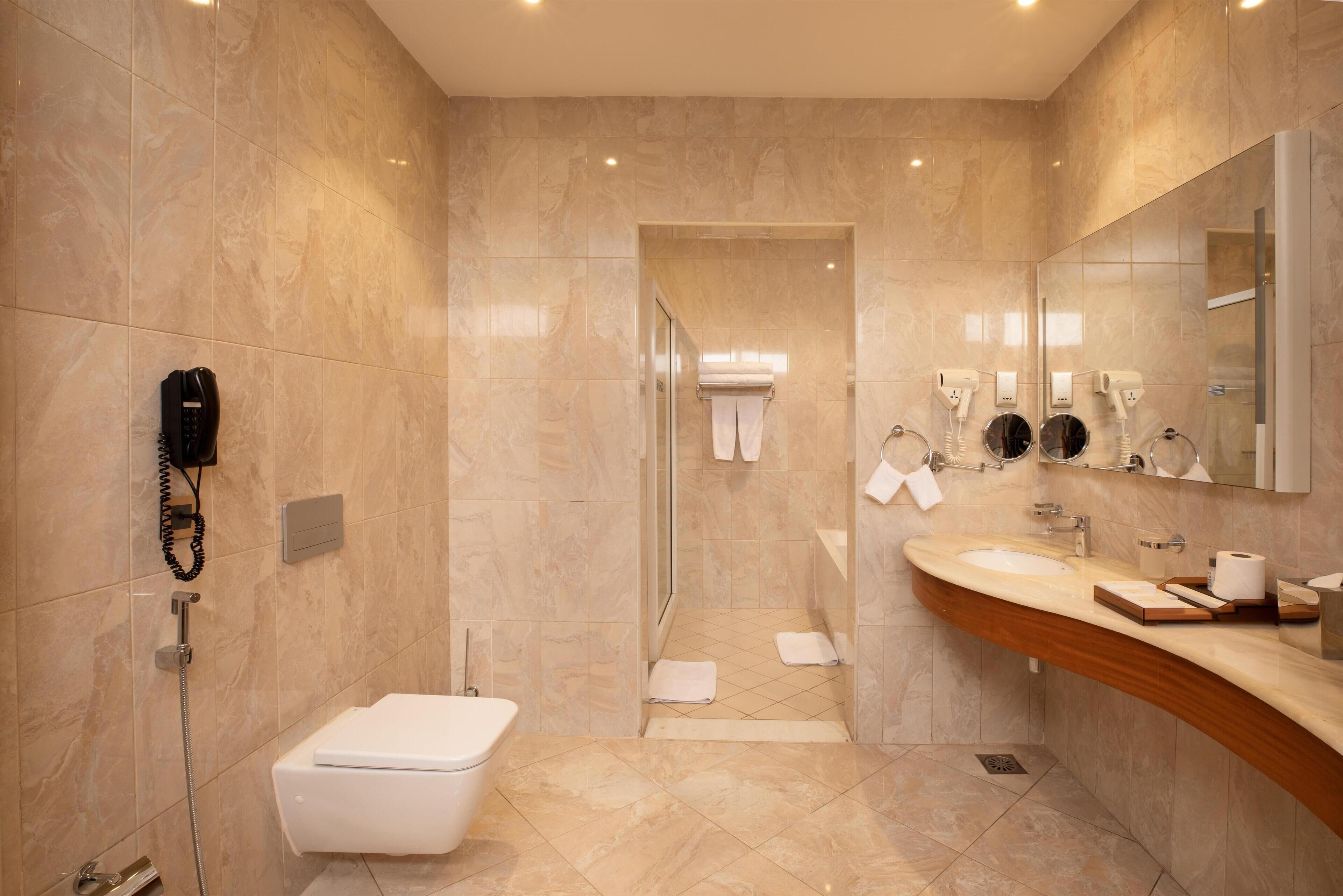 Een moderne badkamer met een marmeren vloer, een wit toilet, een douchegedeelte en een wastafel met spiegel.