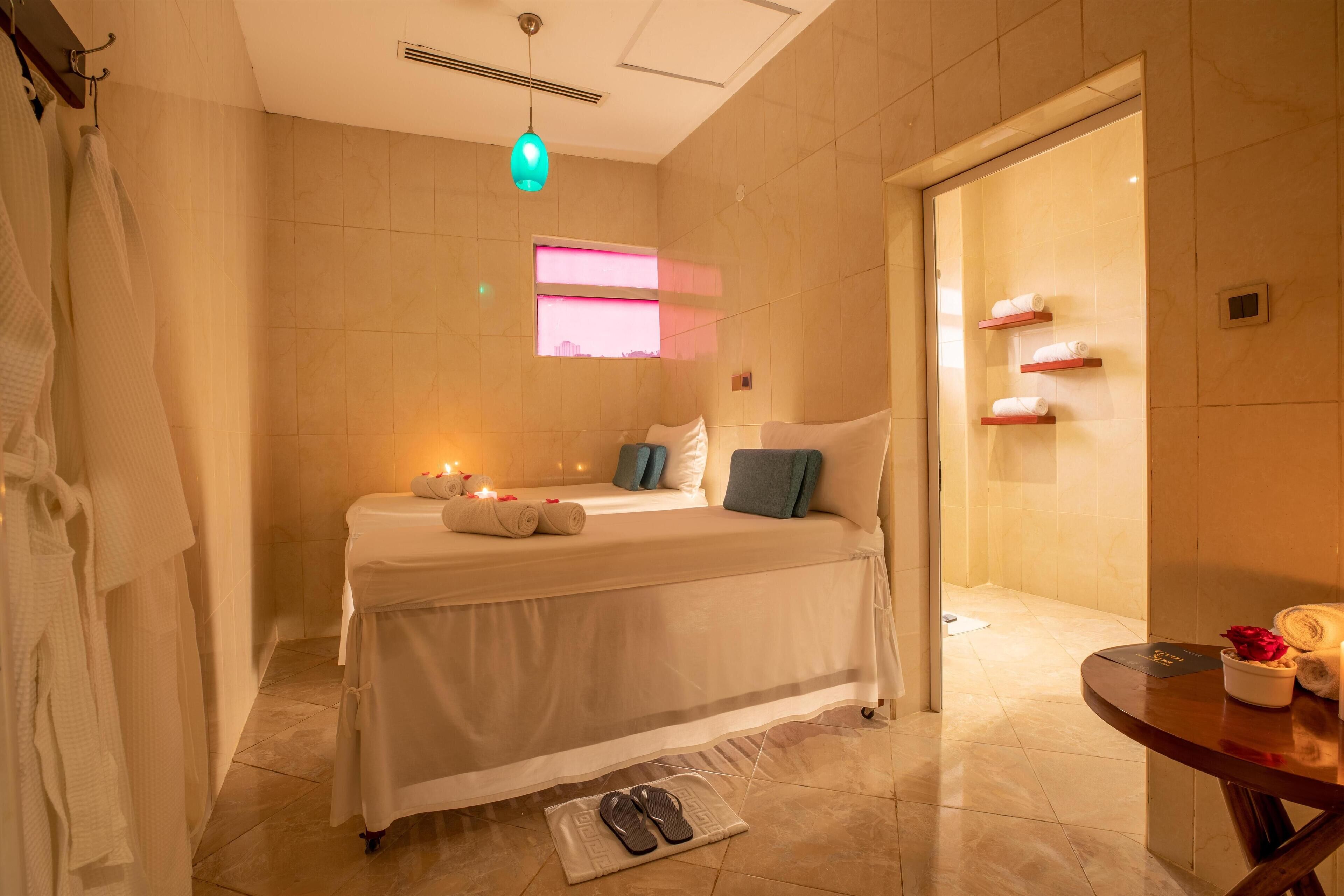 Une chambre d’hôtel avec un lit, une petite table avec des articles de toilette, une fenêtre avec des rideaux roses et un porte-serviettes.