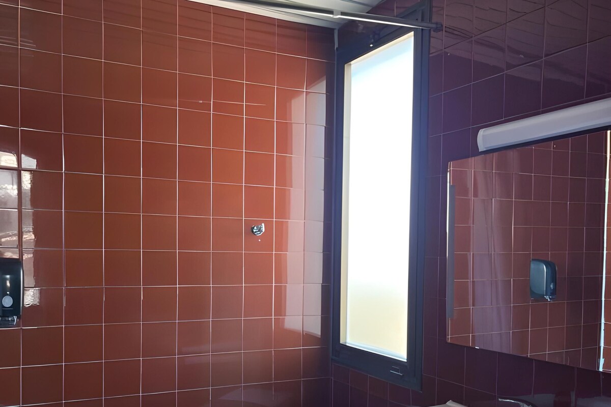 A bathroom with red tiles, a white sink, and a window.