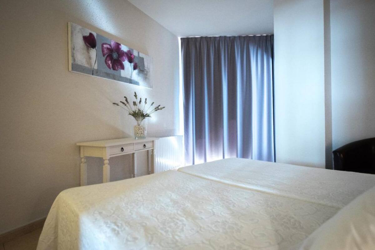 A hotel room with a large bed, a small bedside table with a vase of flowers, and a painting on the wall.