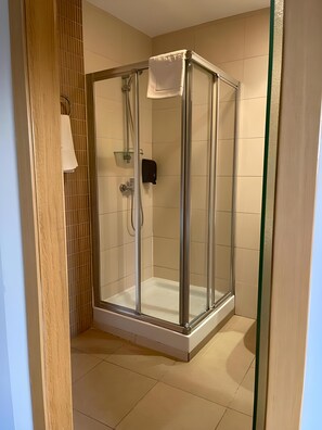A glass-enclosed shower stall with a white towel hanging on the door, a glass shelf, and a black soap dispenser. - Hotel Bruc (El Bruc)