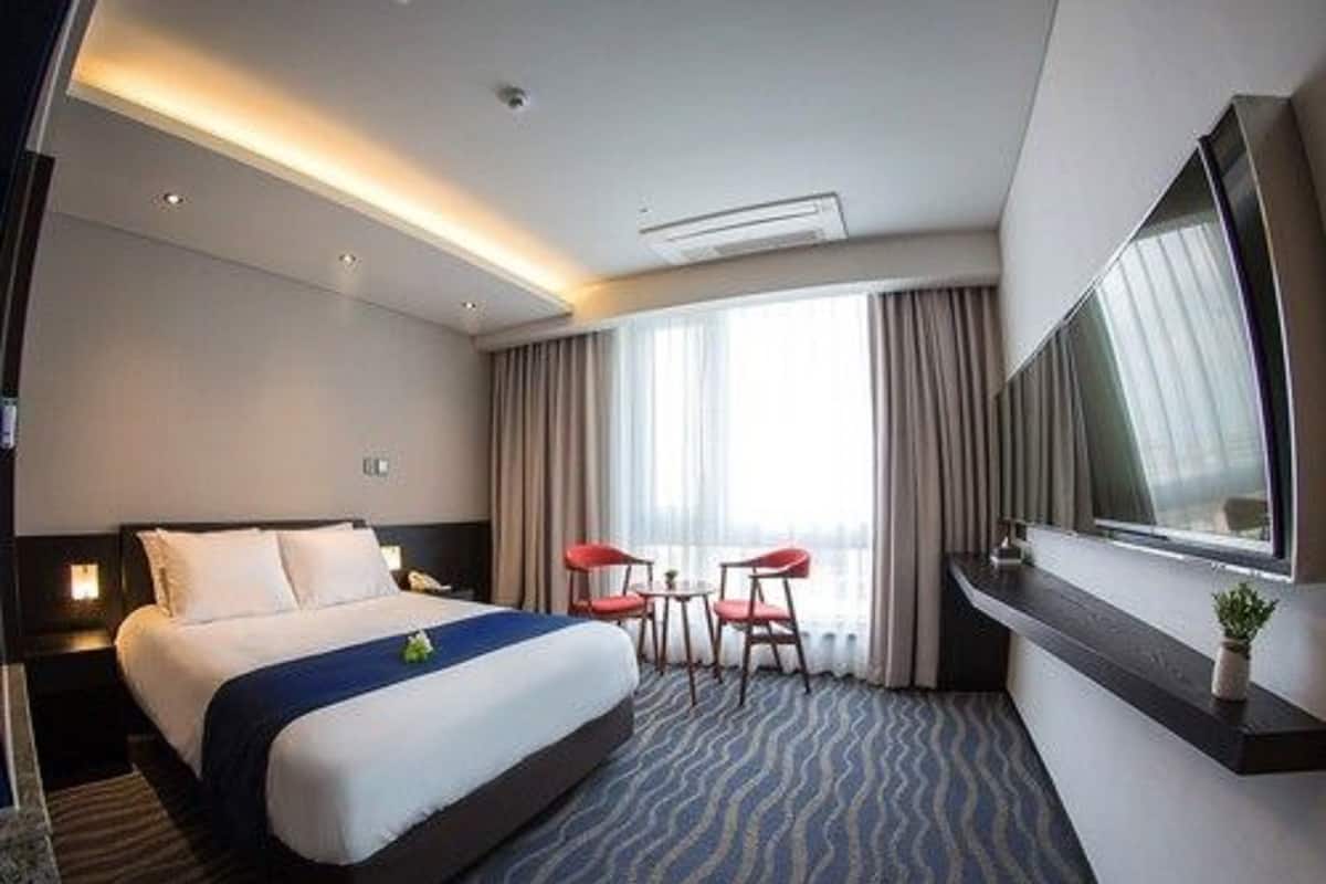 Una habitación de hotel con una cama grande, un escritorio, dos sillas, un televisor y una ventana con cortinas.