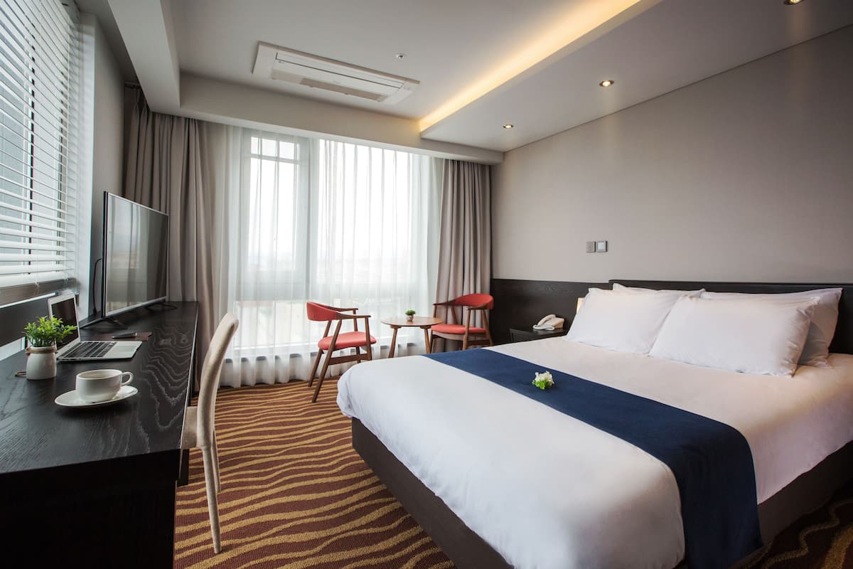 Habitación de hotel con una cama grande, un escritorio con una computadora portátil, un televisor y un área de comedor con sillas.