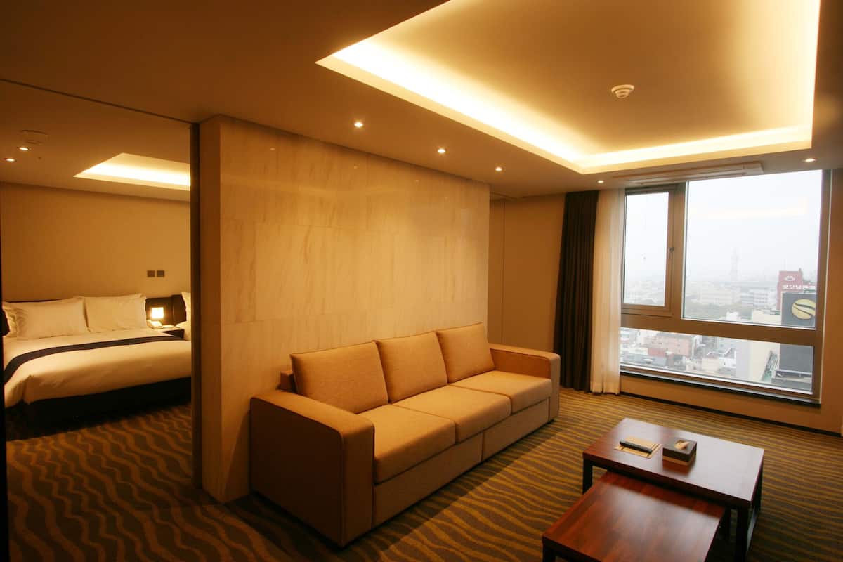 Una habitación de hotel con cama, sofá, una mesita y un ventanal con vistas a la ciudad.