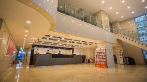 Un vestíbulo amplio con mostrador de recepción, una escalera y barandilla de vidrio.