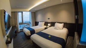 Habitación de hotel con dos camas, televisión, una mesita y vista a la ciudad.