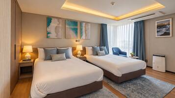 A hotel room with two beds, a desk, a chair, a small table with a plant, and artwork on the walls.