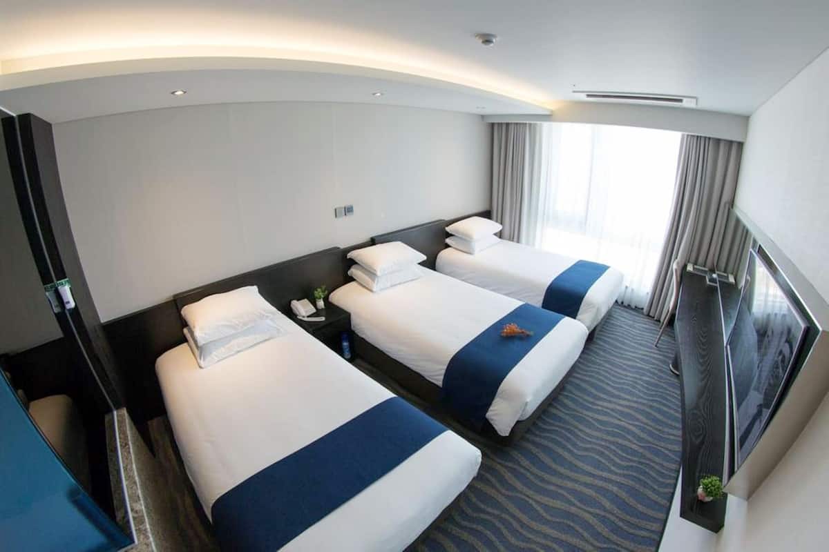 Habitación de hotel con tres camas, un escritorio y un ventanal grande con cortinas.