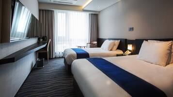 A hotel room with two beds, a desk, a chair, a TV, and a window with curtains.