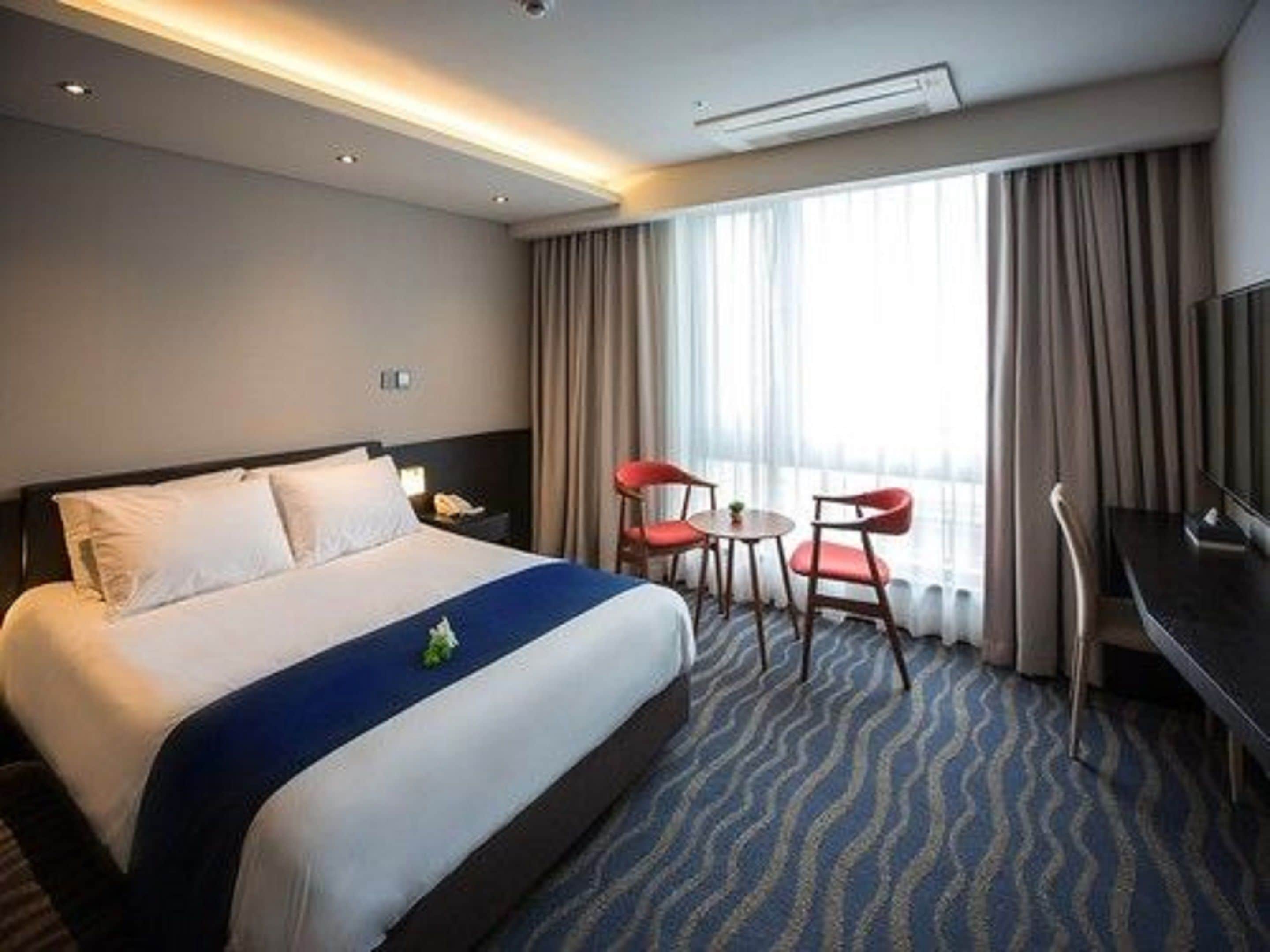 A hotel room with a large bed, a desk with a chair, and a television.