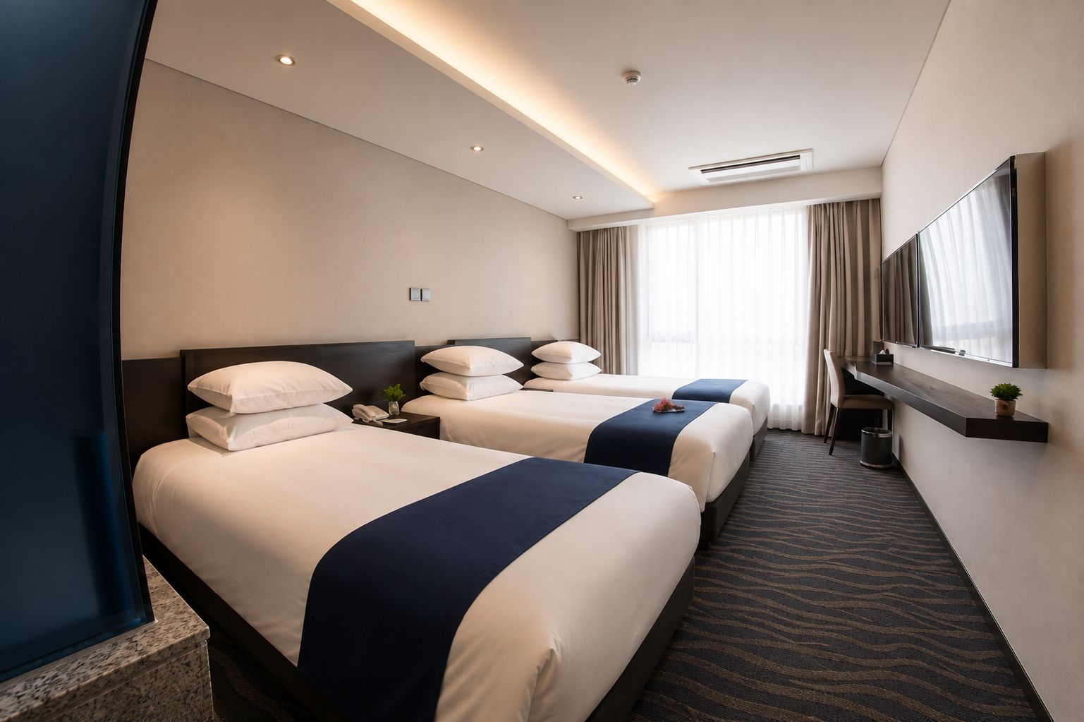 Une chambre d’hôtel avec deux lits, un bureau, une chaise, un miroir et une fenêtre avec des rideaux.