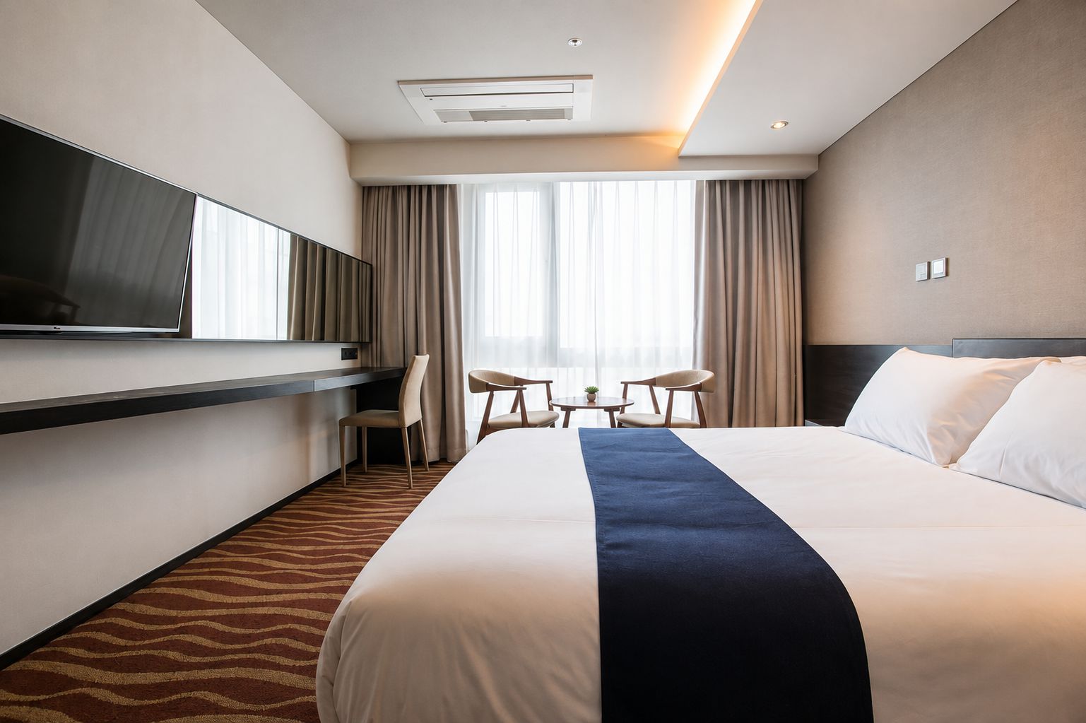 Une chambre d’hôtel avec un lit, une télévision, un bureau et une fenêtre avec des rideaux.