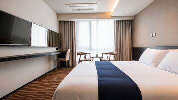 Una habitación de hotel con cama, televisión, escritorio y ventana con cortinas.