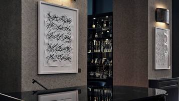 Um interior moderno com arte abstrata nas paredes, área de bar com prateleiras cheias de garrafas e um balcão preto elegante.